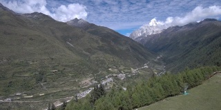 无人机飞向四姑娘山(四姑娘山)，山谷中有一个藏族小村庄(四姑娘山镇)。拍摄于前往海子谷的徒步路线上。