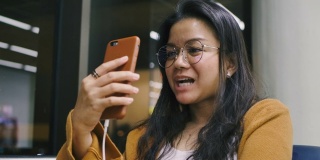 美丽的亚洲年轻女子用她的智能手机视频打电话给朋友或家人，与欢笑快乐的笑脸表情。