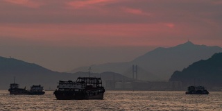 4K延时宽拍摄日落与移动的云在山脉和水上运输物流船船通过海湾。