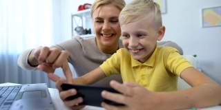 妈妈和小儿子一起玩智能手机上的新游戏，休闲时间，应用程序