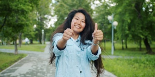 一个快乐的亚洲女人在公园里转头，竖起大拇指的慢动作