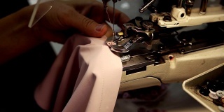 女性的手，一个年轻的裁缝用缝纫机在丝绸衬衫上缝扣子。缝纫机器的按钮。近距离