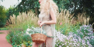 一个成年人，迷人的金发女人走在花园里，穿着灰色的裙子