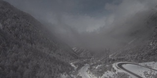 在一个高海拔的山谷里，一架无人机穿过云层降落，山谷下面有一条小路