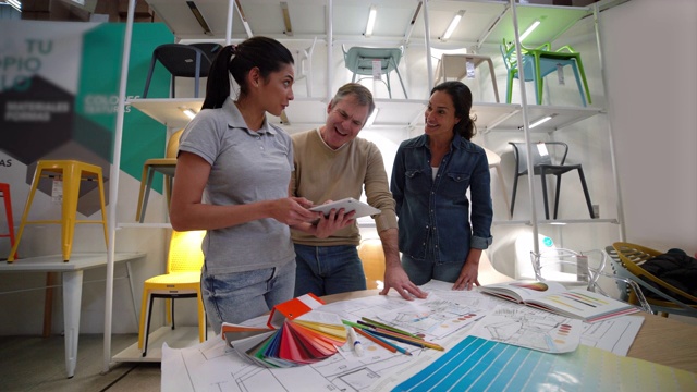 室内设计师拿着平板电脑，向家具店的顾客夫妇建议家居装修项目的颜色
