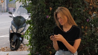 快乐女生利用智能手机语音识别音频ai信息语音功能在以城市城市为背景的街道上行走，语音信息助手学生女生在公园长椅上美丽视频素材模板下载