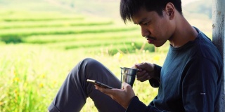 一个男人坐在院子里一边喝茶一边用手机