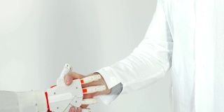 白色背景下穿白大褂的机器人假肢手与人的手握手
