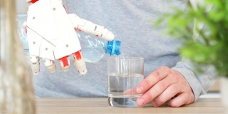 厨房里，一个手持机器人假肢的人正在把瓶子里的水倒进玻璃杯里