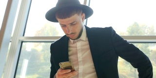 时尚的白人男子穿着黑色西装，戴着帽子，手里拿着手机，在机场看信息，特写，慢动作，商人