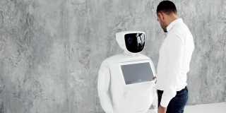 一个时髦的男人与机器人交流，向机器人按一个塑料机械臂，握手。今天控制论系统。现代机器人技术。仿人机器人自主