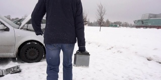 一个男人携带并安装了一个汽车电池在汽车里，冬天。雪,慢动作