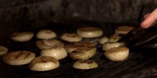 在烤肉架上烹饪薯条切洋葱，或在咖啡馆的煤块上烤洋葱，近距离的洋葱片在餐厅厨房的砖石炉上以慢动作烤
