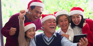 来自不同群体的亚洲人聚集在一起庆祝圣诞节。头发花白的爷爷奶奶，兄弟姐妹，儿子，女儿参加家庭宴会，坐在自制的午餐桌旁，在冷杉树下交谈。