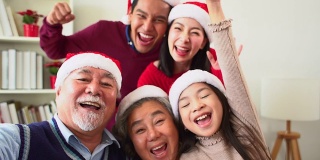 来自不同群体的亚洲人聚集在一起庆祝圣诞节。头发花白的爷爷奶奶，兄弟姐妹，儿子，女儿参加家庭宴会，坐在自制的午餐桌旁，在冷杉树下交谈。
