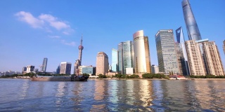 从渡船、摩天大楼和地标建筑上观看上海天际线，以蓝天为背景，船只在黄浦江上航行，4k镜头，慢镜头。