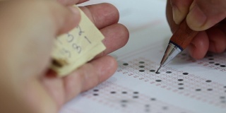 教育的概念。学生手用黑色铅笔画填写标准化考试表格，在答题纸上选择答案，并手拿答题纸进行作弊。