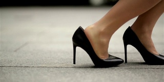 穿着高跟鞋的年轻女商人的脚。女商人下班后穿着高跟鞋在办公室附近散步。慢动作
