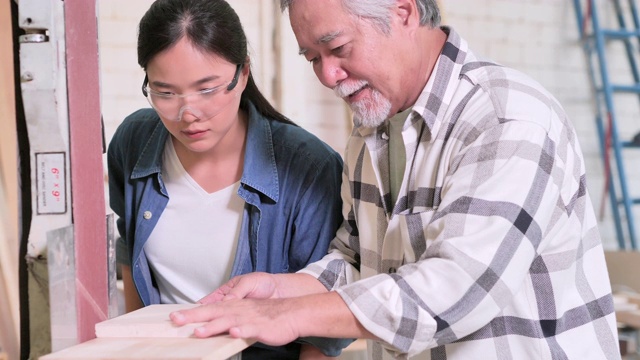亚洲老人木匠教少女与木板在车间。教育，领导力，家庭，人，小企业，领导力，愿景，退休，创新，机会，女性在STEM，蓝领工人的概念