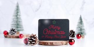 圣诞快乐，新年快乐在黑板松果和装饰圣诞球在白色的桌子和大理石瓷砖墙的背景。简洁简约的风格。假日静物