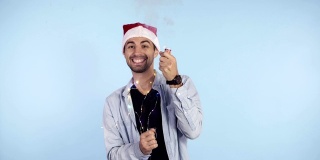 一个穿着休闲衣服，头戴圣诞帽，面带微笑的年轻男子，蓝色背景上的碎纸爆竹会爆炸。庆祝新年或圣诞节的快乐
