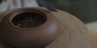 陶工师傅用木柄上的金属铲，用宜兴陶土制作茶壶。茶道用手工陶壶。褐色陶器茶壶。4 k的视频。59.94帧/秒