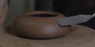 陶工以宜兴陶土为原料，用木轴上的金属铲加工茶壶。茶道用手工陶壶。褐色陶器茶壶。4 k的视频。59.94帧/秒
