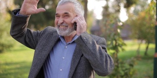 一位快乐的老人在电话里与某人交谈。长着漂亮胡子的帅老头微笑着，高兴极了