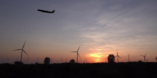 飞机与风力涡轮机在日落。