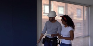 公寓的漂亮黑人女业主与建筑承包商交谈，而他拿着一个剪贴板指着不同的东西