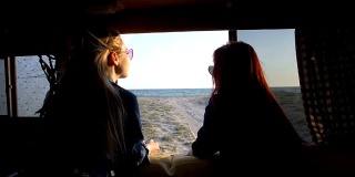 两个女孩从汽车拖车的窗口望向海边