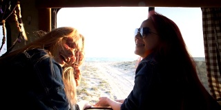 两个女孩在一辆自动拖车的背景下笑着，拖车后面是海岸