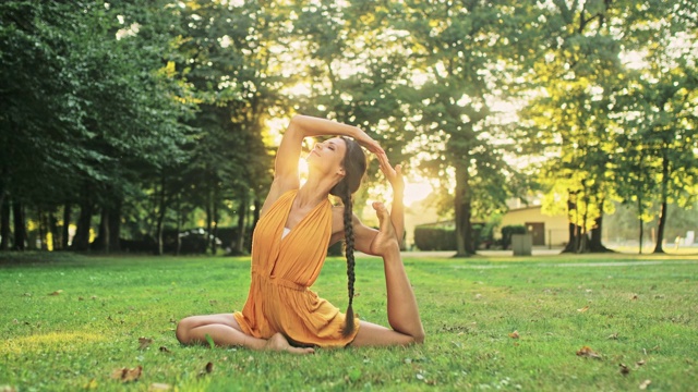 柔韧的年轻女子在阳光公园练习瑜伽