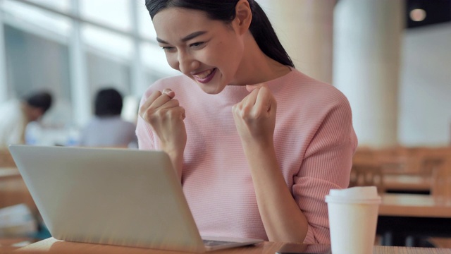 成功的亚洲商务女人高兴地看着笔记本电脑兴奋地表达胜利的姿态，举手是庆祝商业成功的胜利结果。成功、庆祝活动、业务、人员、领导、技术,获得概念。