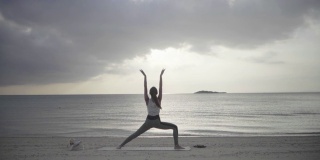 日落时分，一位千禧年妇女在沙滩上练习瑜伽的广角镜头