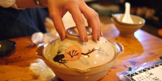 在日本居酒屋餐厅，一名年轻女子正在打开火锅盖