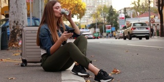 年轻漂亮的女人坐在人行道上用手机找出租车