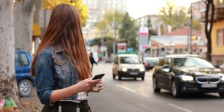 年轻漂亮的女人在人行道上用手机找出租车