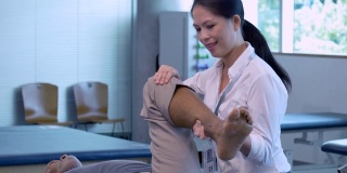 关怀的女性物理治疗师伸展和弯曲一个男性病人的膝盖在会议期间