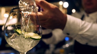 近距离的调酒师测量杜松子酒在一个杯子，把它倒进鸡尾酒杯视频素材模板下载