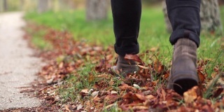 Young man in leather shoes is walking along a path with fallen leaves. Fall season. Outdoor city walk concept slow motion.