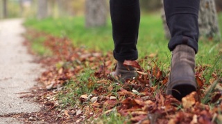 Young man in leather shoes is walking along a path with fallen leaves. Fall season. Outdoor city walk concept slow motion.视频素材模板下载