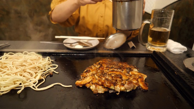 在日式餐厅里，一名年轻女子正在往御好烧里加酱