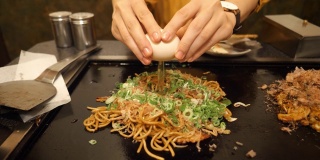 在日式餐厅里，年轻女子把鸡蛋放在日式炒面上