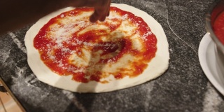 厨师在披萨上亲手浇上番茄酱和帕尔马干酪