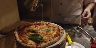 披萨师在新鲜出炉的那不勒斯披萨上浇上新鲜罗勒和橄榄油