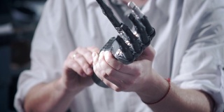 一位科学家工程师正在测试一个电子仿生假肢。他移动机械手臂的塑料手指。现代修复技术。科学家手中的控制论之手