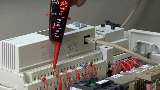 工厂工人的手检查电子设备的触点电压指示器。