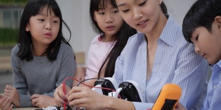 亚洲女教师在学校的实验室教学和测试机器人反应。年轻的建筑师孩子们设计和演示电路技术想法和协作开发机器人。