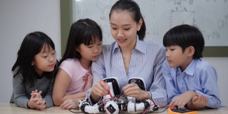 亚洲女教师在学校的实验室教学和测试机器人反应。年轻的建筑师孩子们设计和演示电路技术想法和协作开发机器人。